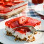 A close-up of a fork cutting through the pretzel crust of a strawberry salad slice.