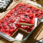 A glass baking dish of strawberry pretzel salad with a slice being lifted out by a spatula.