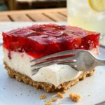 A close-up of a fork breaking through the pretzel crust of a strawberry salad slice.