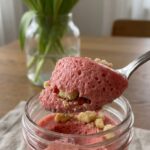 A close-up of a spoon lifting a scoop of fluffy pink mousse from a glass.