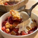 A close-up of a spoon lifting a bite of cake with rhubarb filling and melting vanilla ice cream.