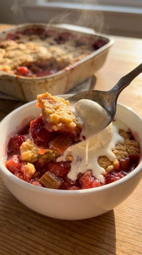 A close-up of a spoon lifting a bite of cake with rhubarb filling and melting vanilla ice cream.