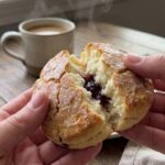 A close-up of hands breaking open a warm, steaming strawberry biscuit revealing the soft inside.