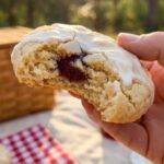 A close-up of hands breaking a soft strawberry cookie in half, revealing the moist interior.