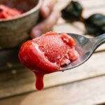 A close-up of a spoon taking a scoop of melting strawberry sorbet.