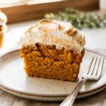 A close-up cross-section of a halved sweet potato cupcake, showing a moist orange interior and fluffy toasted marshmallow frosting.
