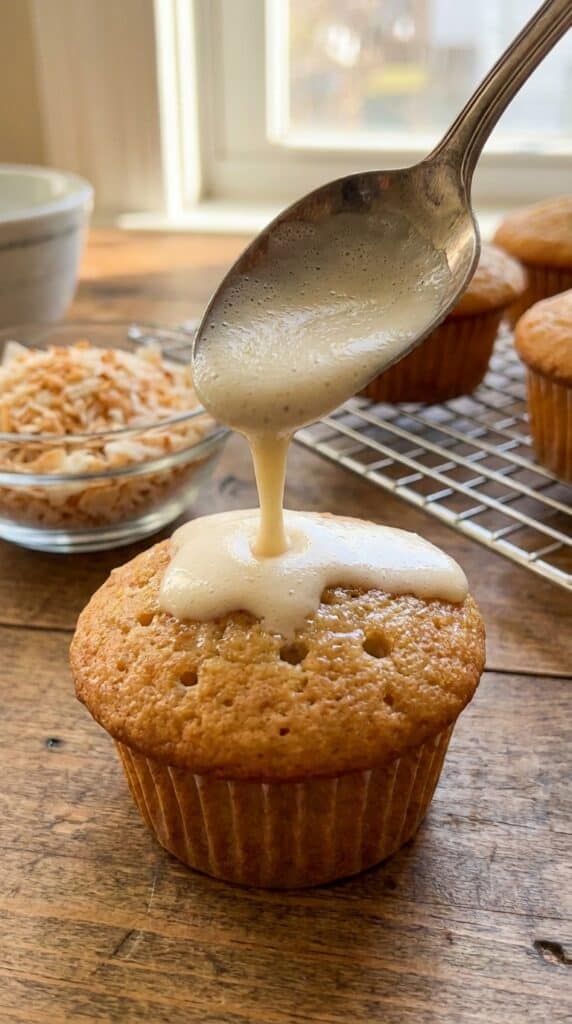 A close-up of a spoon pouring creamy milk over a poked cupcake so it can soak into the sponge