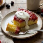 A slice of warm upside-down strawberry cake with melting whipped cream on a plate.