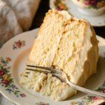 A close-up of a fork cutting into a slice of moist vanilla cake on a floral plate.