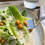 A close-up of a fork lifting a bite of romaine lettuce coated in creamy dressing with roasted chickpeas.