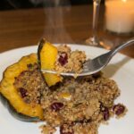 A close-up of a fork lifting a bite of roasted acorn squash and quinoa filling with steam rising.
