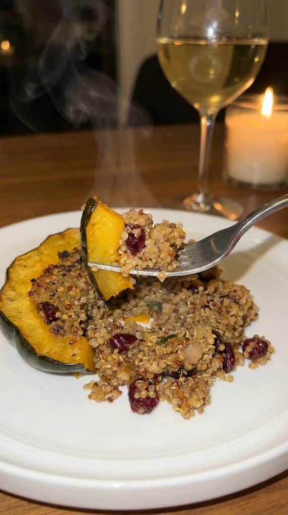 A close-up of a fork lifting a bite of roasted acorn squash and quinoa filling with steam rising.
