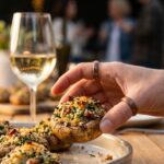 A close-up of a hand picking up a single crispy stuffed mushroom from a tray at a party.