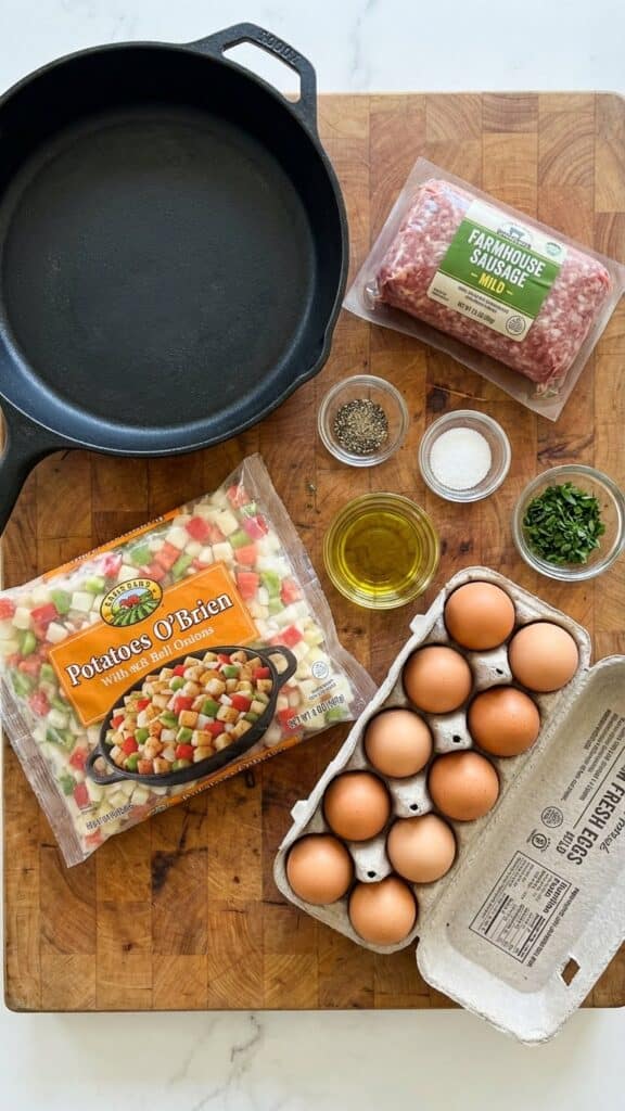 A flat lay showing a package of sausage, a bag of frozen potatoes with peppers, and a carton of eggs next to a skillet.