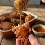 A close-up POV shot of spicy honey being drizzled over a piece of crispy baked chicken.