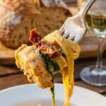 A close-up of a fork lifting a bite of creamy chicken and pasta with sun-dried tomatoes.