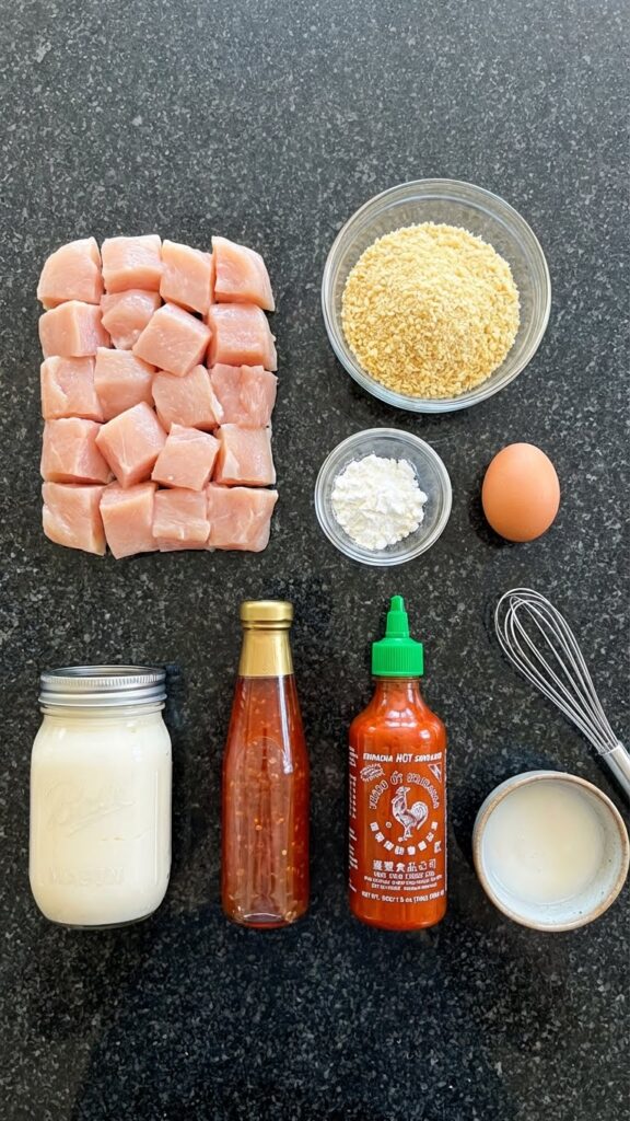 Overhead flat lay of ingredients for Bang Bang Chicken: raw chicken, panko, mayo, sweet chili sauce, and sriracha.