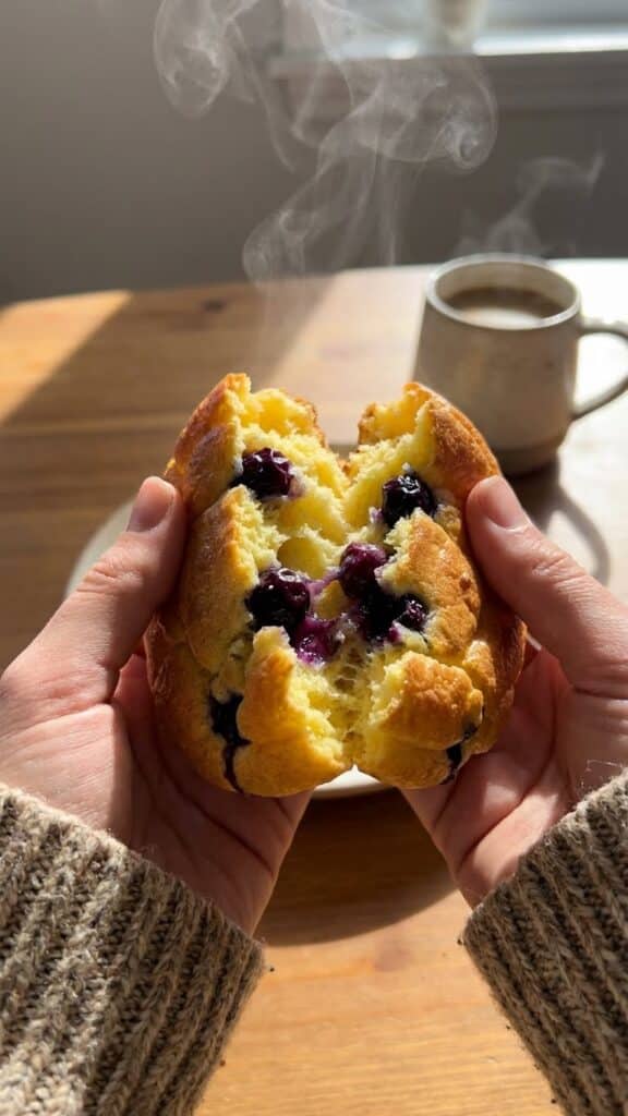 A close-up of hands tearing open a piece of fluffy blueberry cloud bread, showing the airy texture inside.