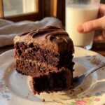 A close-up of a fork cutting through a slice of chocolate mousse cake, showing the soft mousse and dense brownie textures.