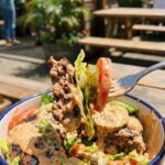 A close-up POV shot of a fork lifting a mixed bite of burger patty, lettuce, pickle, and sauce from a bowl.