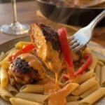 A close-up of a fork lifting creamy cajun chicken and peppers over pasta.