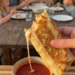 A close-up of a hand dipping a crispy cheesy chicken wrap into a bowl of red marinara sauce.