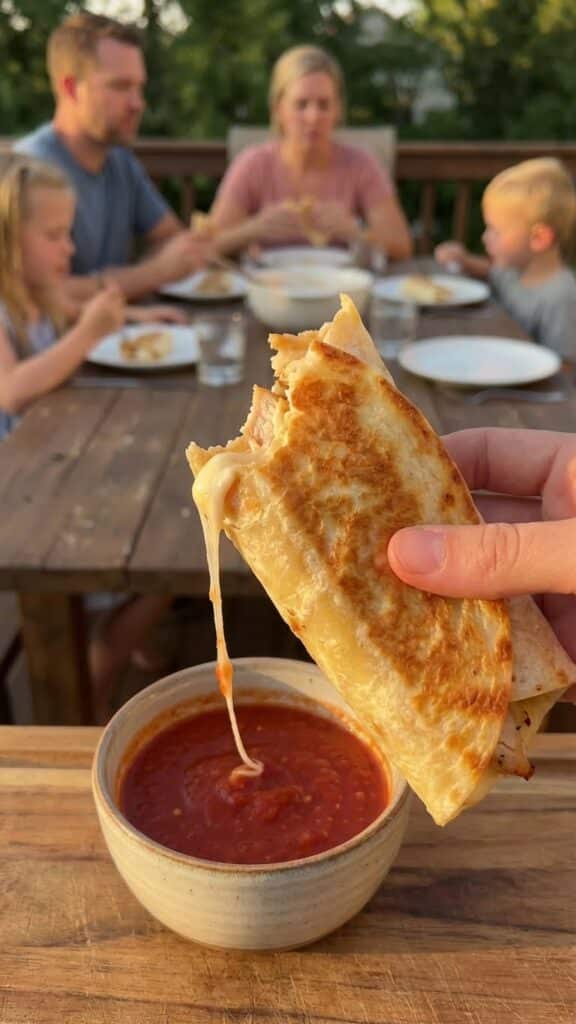 A close-up of a hand dipping a crispy cheesy chicken wrap into a bowl of red marinara sauce.