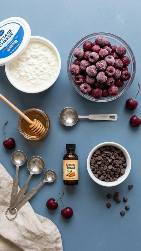 A flat lay showing cottage cheese, frozen cherries, honey, almond extract, and chocolate chips.