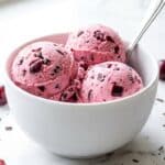 A close-up of an ice cream scoop forming a ball of pink cherry ice cream from a loaf pan.