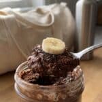 A close-up of a spoon lifting thick chocolate oats and banana from a jar.