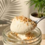 A close-up of a spoon lifting a bite of smooth coconut mousse, showing the thick creamy texture.