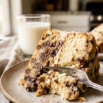 A close-up of a slice of cookie dough cake with a fork cutting through the dough layer.