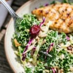 A close-up of a fork lifting a bite of crunchy kale salad with dressing and seeds.