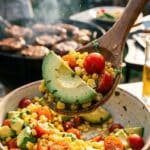 A close-up of a wooden spoon lifting a scoop of corn, tomato, and avocado salad.