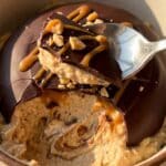 A close-up of a spoon cracking a hard chocolate shell to reveal smooth peanut butter filling.