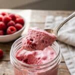 A close-up of a spoon lifting a scoop of fluffy pink raspberry mousse.