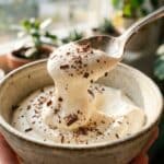 : A close-up of a spoon lifting a thick dollop of vanilla mousse with chocolate shavings.
