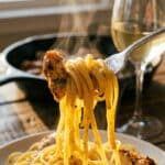 A close-up of a fork lifting a saucy bite of linguine and chicken, dripping with golden butter sauce.