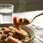 A close-up of a fork lifting a bite of quinoa salad with apple and cranberry.