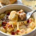 A close-up of a spoon lifting a creamy gnocchi dumpling and chicken from a bowl with bacon topping.