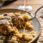 A close-up of a fork lifting a bite of chicken and rice coated in creamy onion gravy.