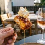 A close-up POV shot of a fork holding a piece of crispy chicken dripping with hot honey and topped with feta cheese.