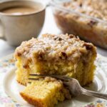 A close-up of a square slice of pineapple cake with coconut pecan frosting on a floral plate with a fork.