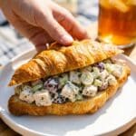 A buttery croissant sandwich filled generously with chicken salad and grapes on a plate.