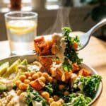 A close-up of a fork lifting a bite of sweet potato and kale covered in creamy dressing.