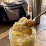 A close-up of a spoon lifting a bite of creamy banana pudding with a softened cookie.
