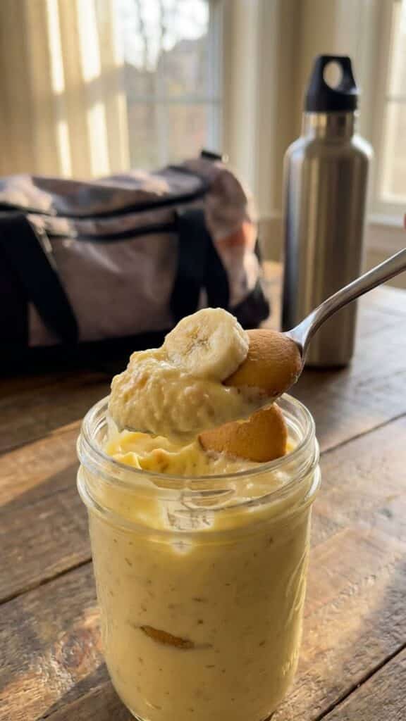 A close-up of a spoon lifting a bite of creamy banana pudding with a softened cookie.
