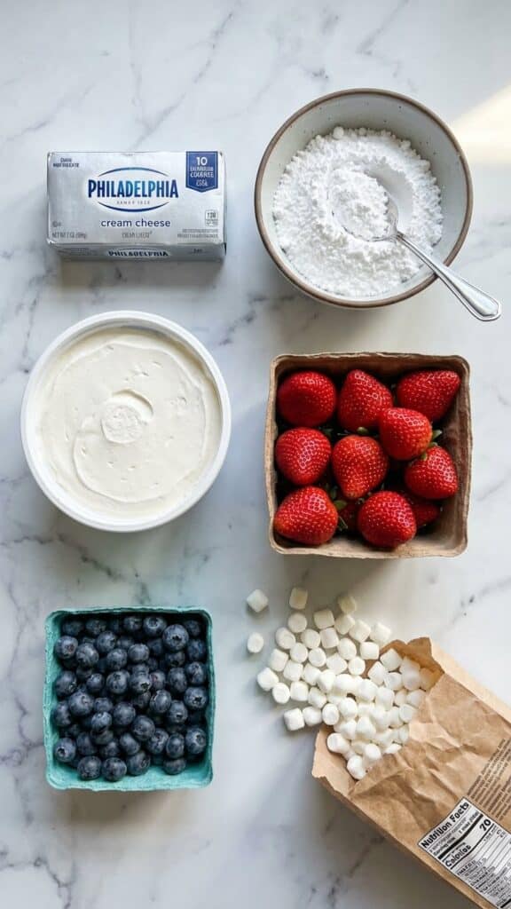 A close-up of a spoon lifting a bite of creamy strawberry and blueberry cheesecake salad from a small white bowl.