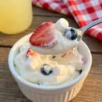 An overhead flat lay of ingredients including cream cheese, cool whip, strawberries, blueberries, and marshmallows on a marble surface.