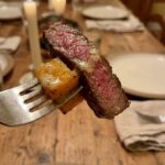 A close-up POV shot of a fork holding a slice of garlic butter steak and roasted butternut squash glistening with sauce.